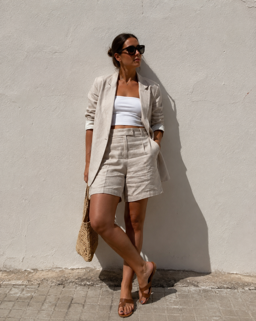 Woman in a beige tailored linen short suit leaning against a stucco wall, summer work outfit