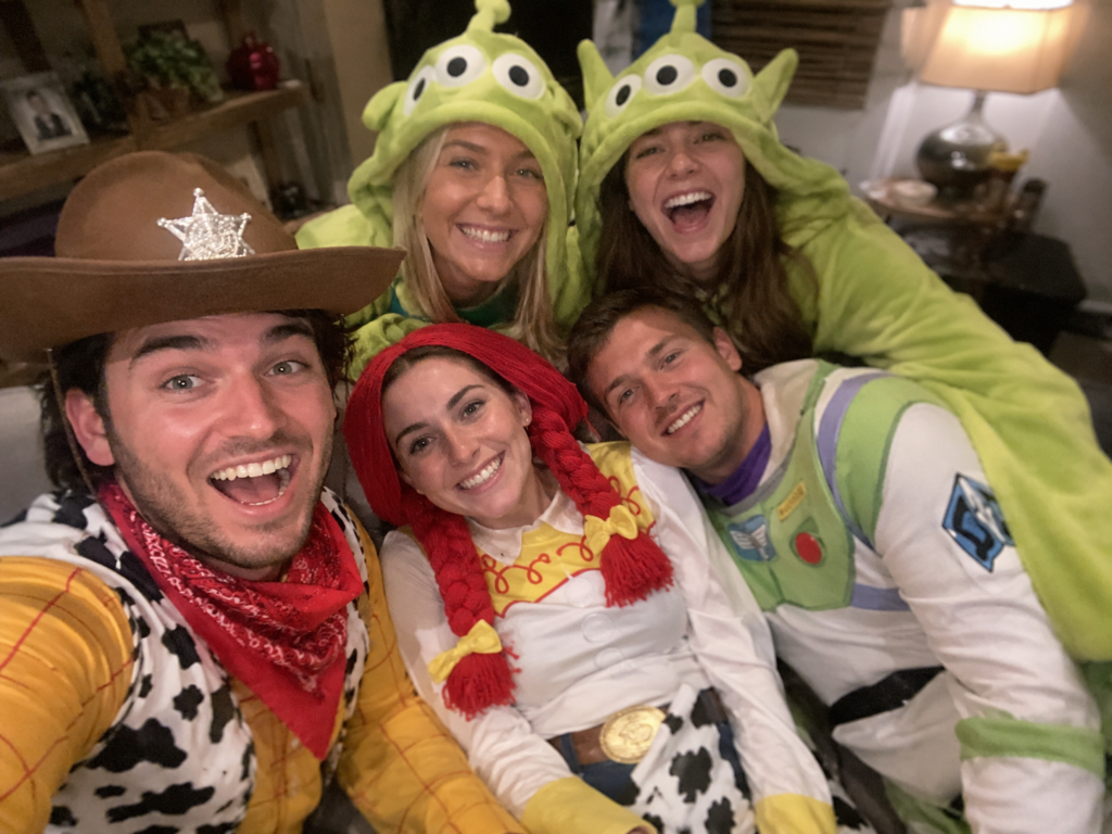 Group of friends in toy-inspired costumes - cowboy, cowgirl, space ranger, and green aliens - piled on a couch, Disney Halloween costume idea