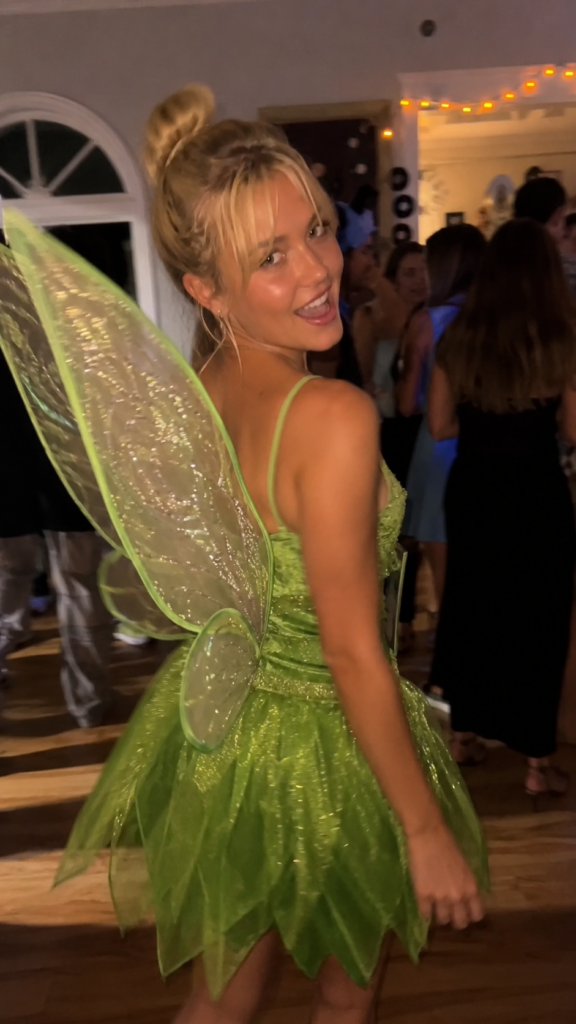 Woman in a short green dress with fairy wings caught mid-twirl, Tinker Bell Disney Halloween costume