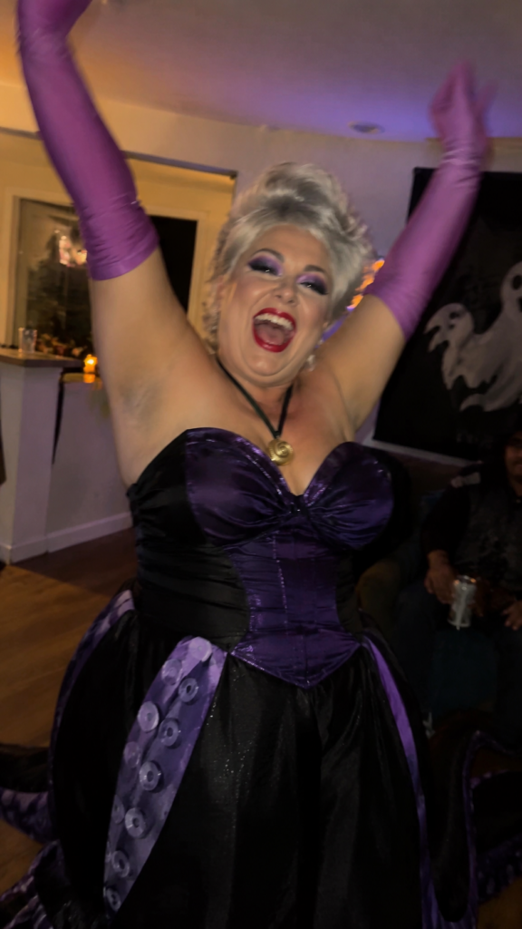 Woman in a bold purple-and-black costume with silver hair dancing, Ursula Disney Halloween costume