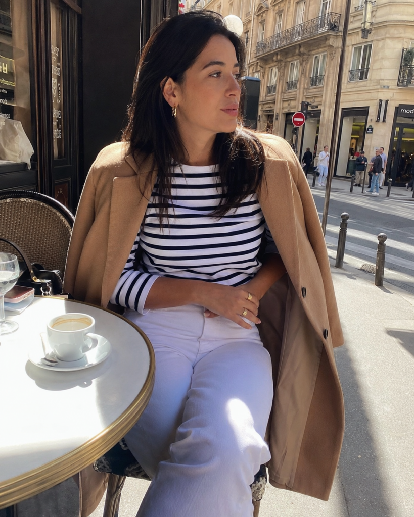 Woman in white jeans, navy striped top, and camel blazer at an outdoor cafe, summer work outfit