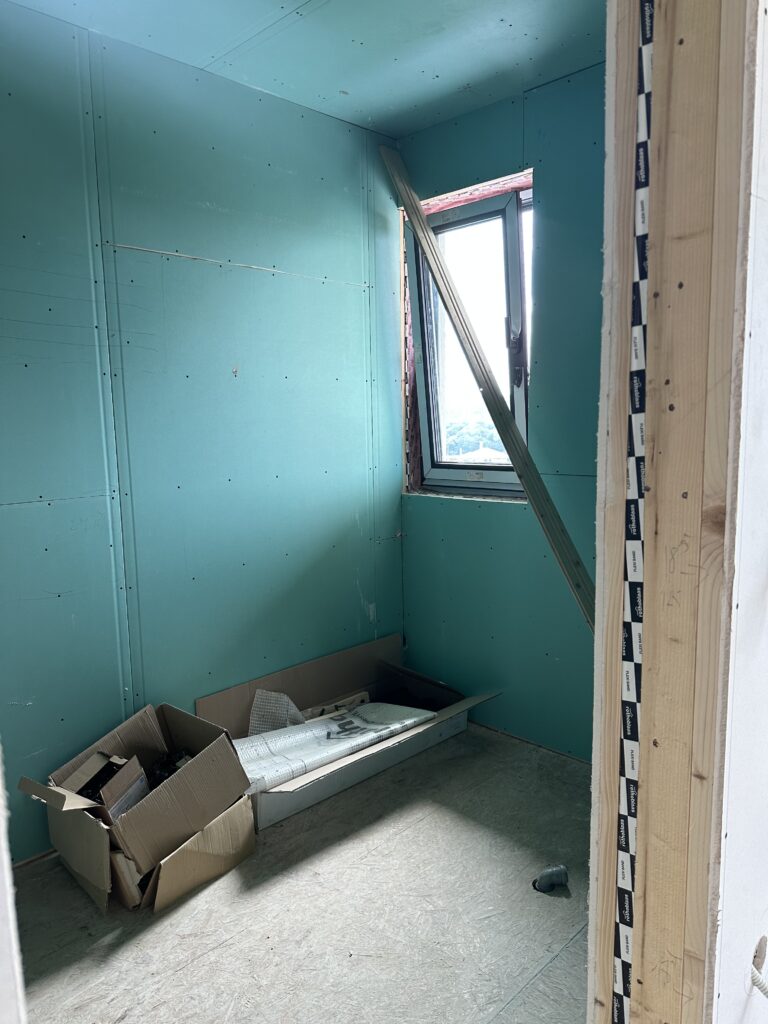 Small bathroom finished with green moisture-resistant drywall and a black-framed window, with an empty box on the subfloor