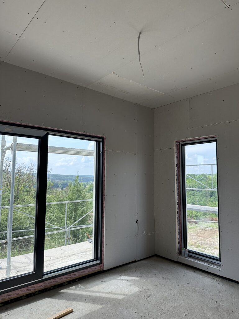 First-floor bedroom drywalled, with a large window and a tall narrow window framing the countryside view
