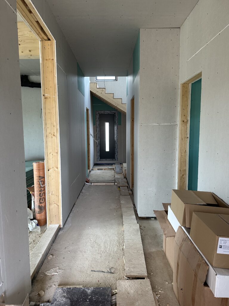 Long hallway with grey and green drywall, looking toward the black entry door with a vertical glass strip