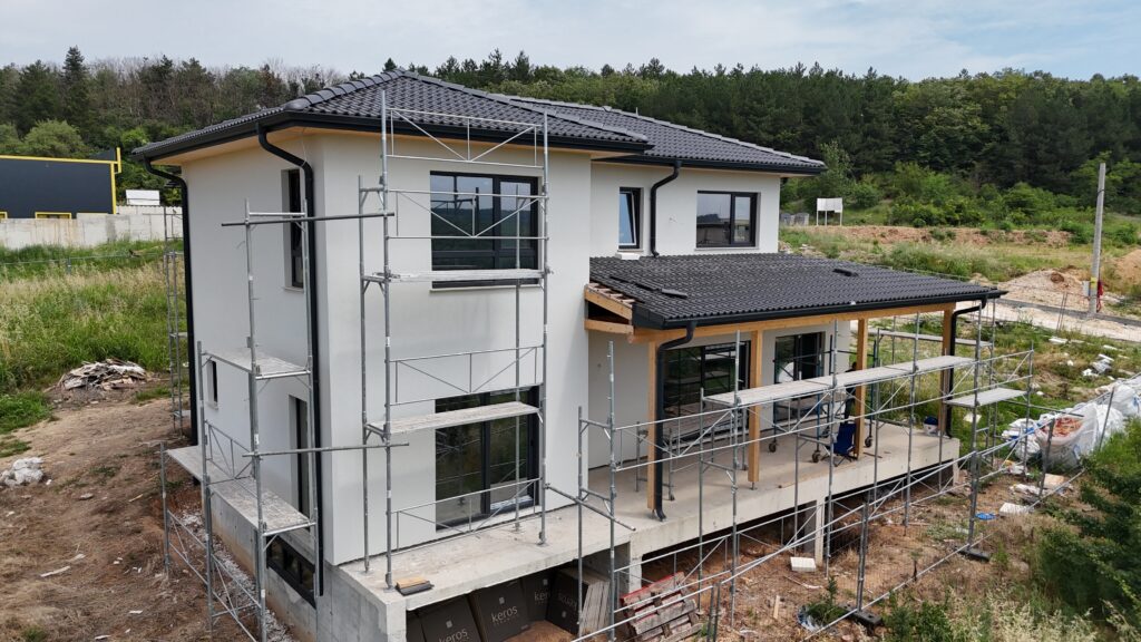 Modern house exterior in warm white with black windows, wood soffits, and scaffolding