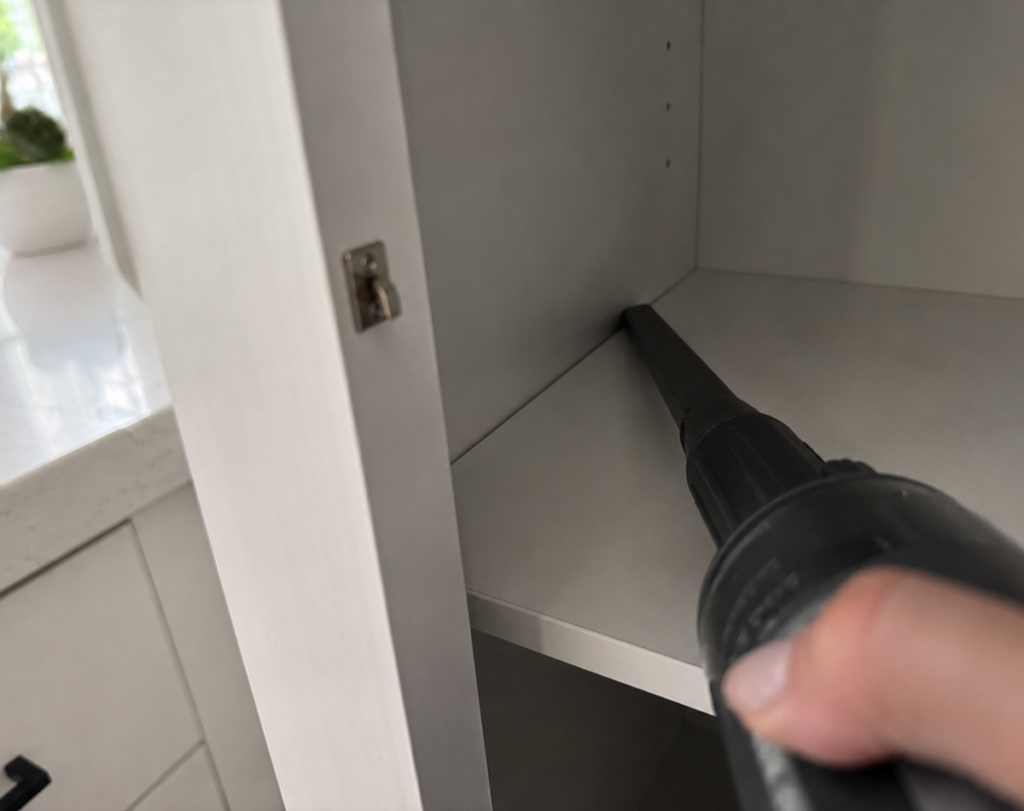 Vacuuming the corners and cracks of an empty pantry shelf to remove pantry moth eggs and larvae
