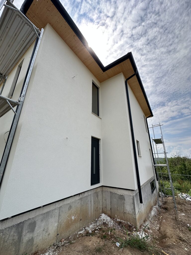 Warm white exterior color with black windows, wood soffits, and unfinished concrete plinth