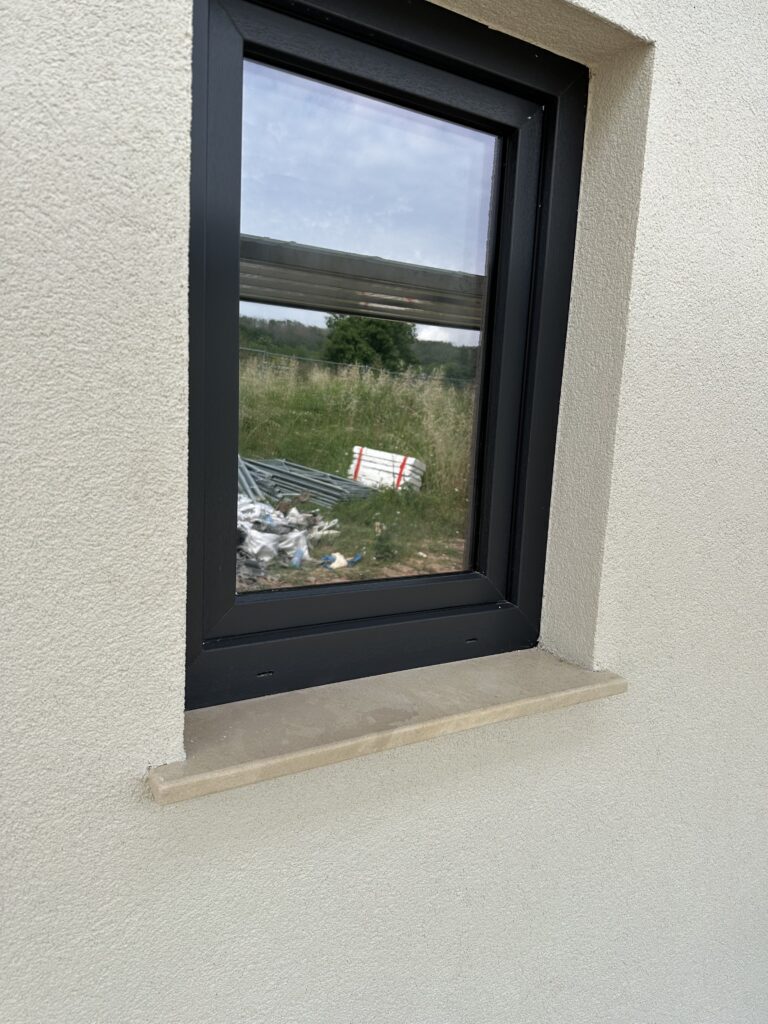 Black window frame with limestone sill against a warm white exterior wall