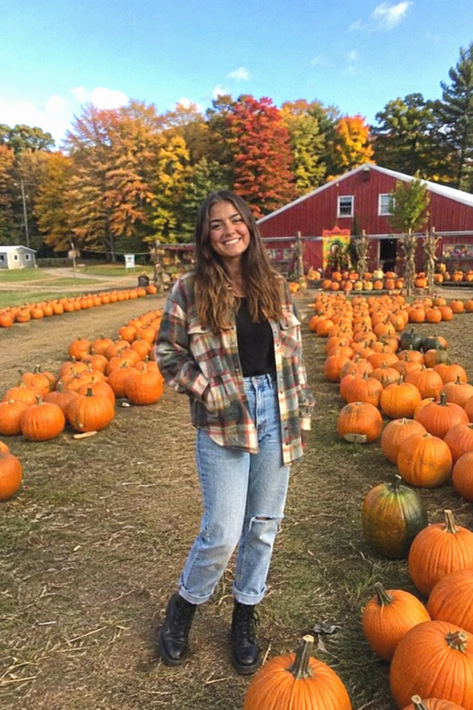 Woman in a plaid flannel shacket and jeans at a pumpkin patch on a sunny fall day