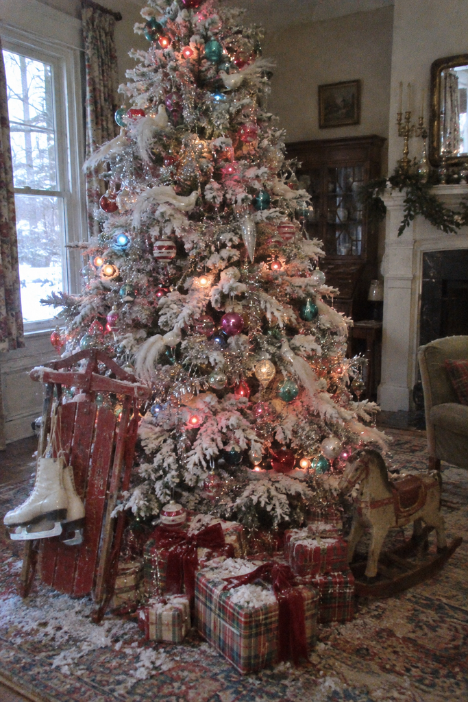 Snow-flocked Christmas tree decorated with colorful vintage glass ornaments, silver tinsel, and wrapped holiday gifts